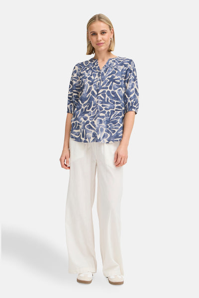 Blauwe blouse met korte mouwen van Fransa, met abstracte patronen, gedragen met een witte broek met wijde pijpen.