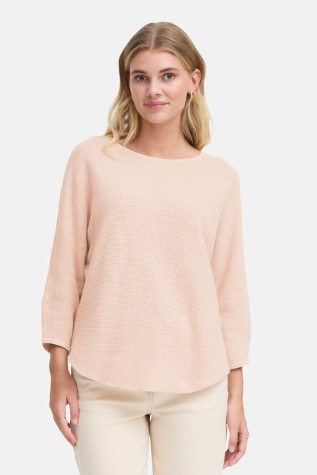 Pull à col rond rose de Fransa®, en tricot côtelé, porté avec un pantalon blanc cassé.
