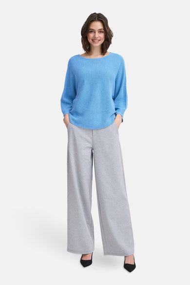 Pull à col rond bleu de Fransa, porté avec un pantalon gris large et des escarpins noirs.