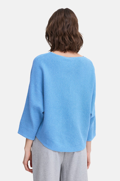 Pull bleu à col rond de Fransa, en maille texturée, porté avec un pantalon gris, vue de dos.
