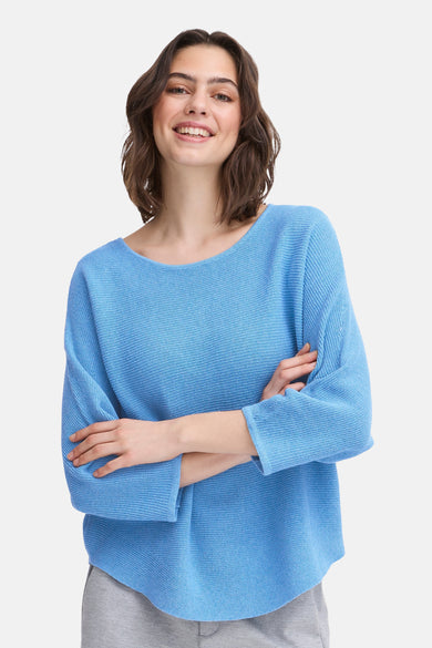 Pull à col rond bleu de Fransa, porté par un modèle souriant avec les bras croisés.