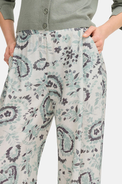 Groene broek met bloemenprint van Fransa, gedragen met een gebreid vest met knopen, handen in de zakken.