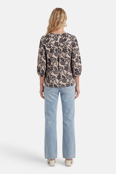 Blouse fleurie noire et beige de Fransa®, à manches 3/4 bouffantes, vue de dos, portée avec un jean clair et des mules beiges.