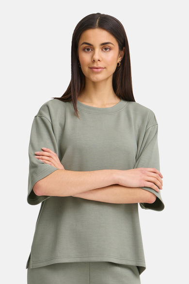 Groene sweater uit Frankrijk, korte mouwen en een losse pasvorm, gedragen met gouden oorringen.