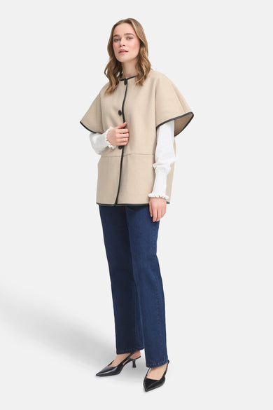 Veste beige Fransa® avec bordure noire, portée sur un chemisier blanc à volants et un jean bleu.