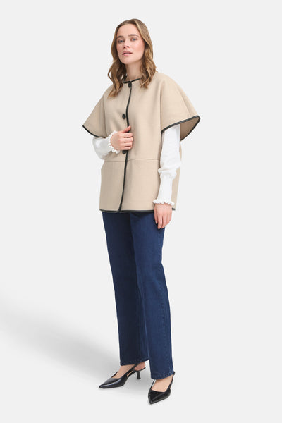 Veste beige Fransa® avec bordure noire, portée sur un chemisier blanc à volants et un jean bleu.