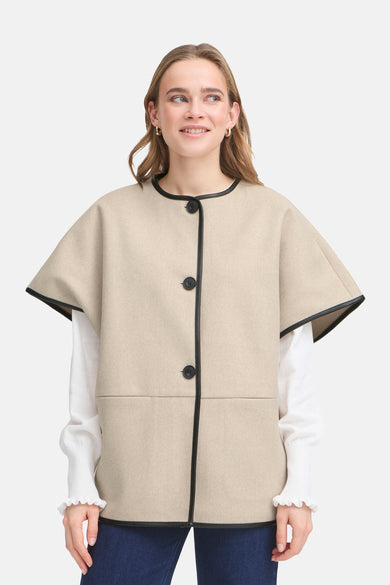 Veste beige, de Fransa, avec boutons et col en cuir noir, portée sur un chemisier blanc à manches longues.
