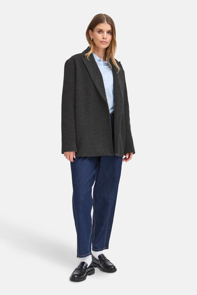 Veste courte grise de Fransa, portée sur une chemise bleu clair et un jean décontracté, avec des mocassins noirs.

