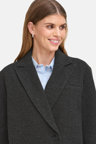 Veste courte grise de Fransa, portée sur une chemise bleu clair boutonnée.