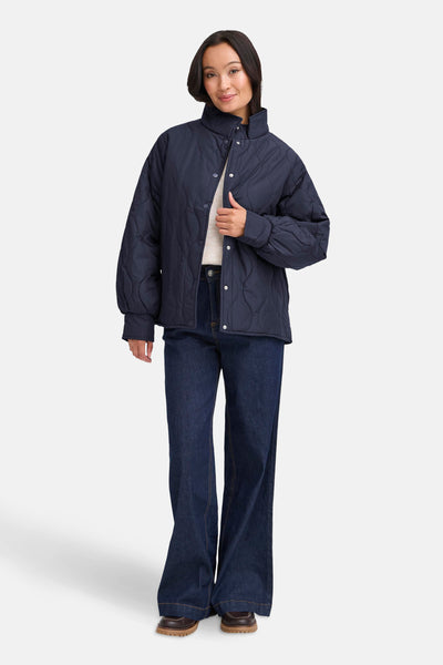 Veste courte bleue de Fransa, matelassée avec une fermeture boutonnée, portée sur un pull crème et un jean évasé.