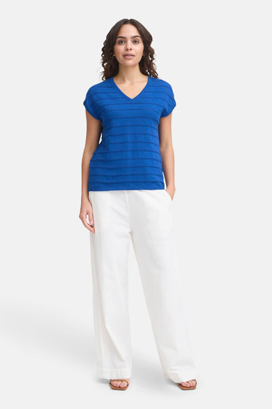 T-shirt bleu à manches courtes de Fransa, porté avec un pantalon blanc ample et des sandales marron.
