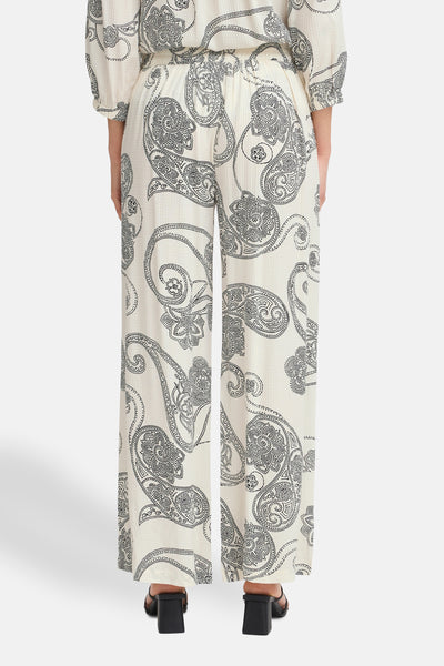 Pantalon écru à motif cachemire de Fransa, coupe ample et jambes larges, porté avec des chaussures noires à talons.
