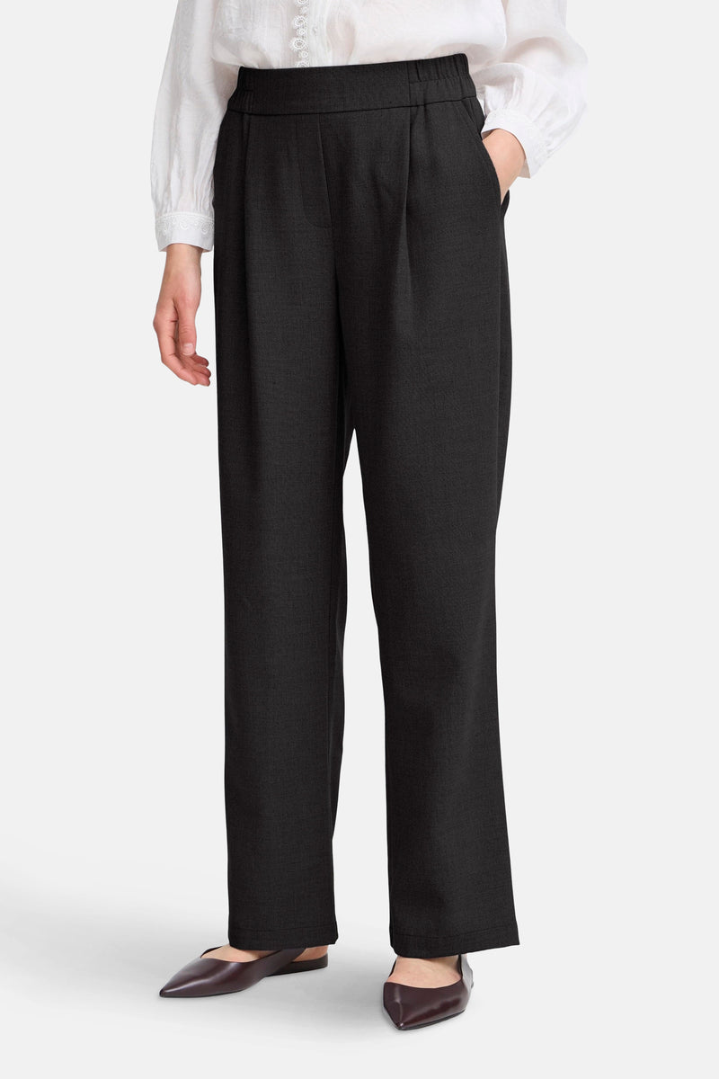 Pantalon noir de Fransa, coupe ample avec plis, porté avec une blouse blanche et des chaussures pointues.
