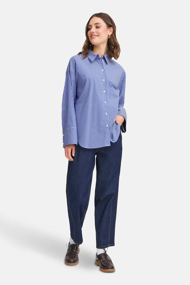 Blauwe blouse met verticale strepen van Fransa, gedragen met een wijde spijkerbroek en bruine veterschoenen.