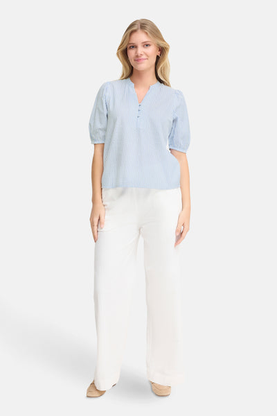 Chemisier bleu à rayures de Fransa, porté avec pantalon blanc et chaussures en daim.
