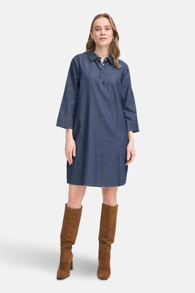 Robe en denim bleu foncé de Fransa, avec col chemise et manches trois-quarts, portée avec des bottes marron.
