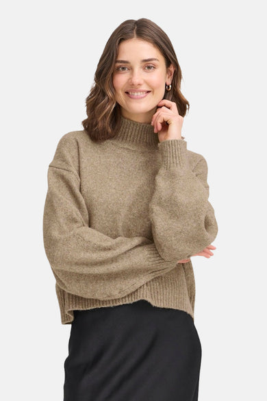 Beige coltrui van Fransa, gedragen met een zwarte rok en gouden oorbellen.