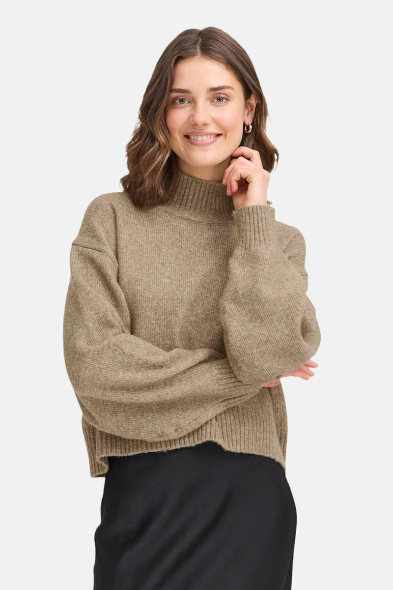 Beige coltrui van Fransa, gedragen met een zwarte rok en gouden oorbellen.