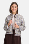 Multicolored floral-patterned women's casual jacket with brown trim and front buttons, worn over a beige top and dark skirt, front view