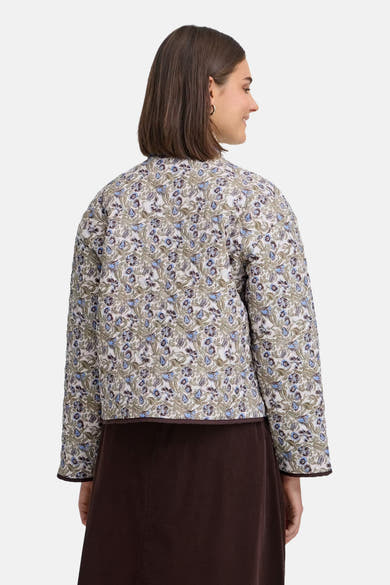 Multicolored floral patterned casual jacket back view with brown trim and quilted texture worn with dark skirt