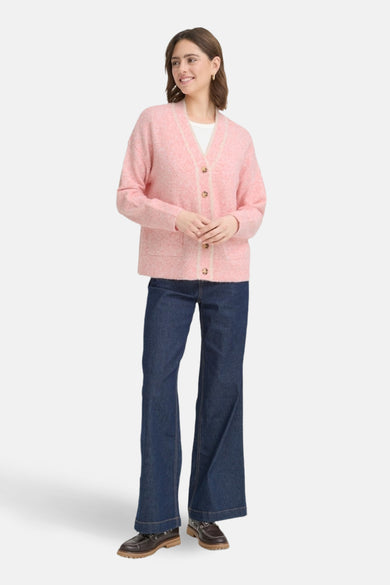 Roze gebreid vest uit Frankrijk, met knopen en contrasterende afwerkingen, gedragen over een wit T-shirt en een blauwe jeans.