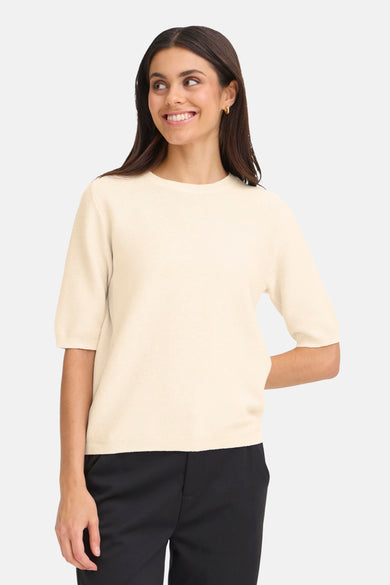Pull à col rond beige de Fransa, porté avec un pantalon noir.