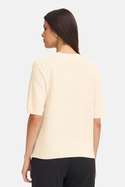 Pull à col rond beige de Fransa, manches courtes, texture maille discrète, porté avec un pantalon noir.
