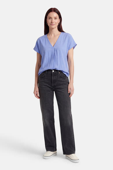Blouse bleue à manches courtes de Fransa, avec col en V et plis sur le devant, portée avec un jean gris.