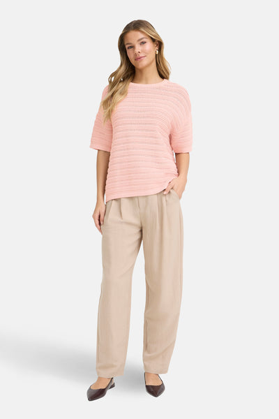 Pull à col rond rose de Fransa, à mailles ajourées horizontales, porté avec un pantalon beige ample.
