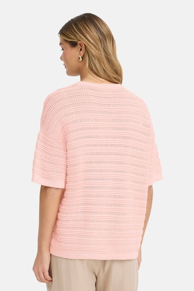 Pull à col rond rose de Fransa, avec une maille ajourée à rayures horizontales, porté avec un pantalon beige.