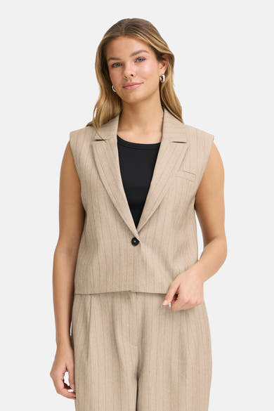 Beige blazer uit Frankrijk, mouwloos model met fijne strepen, gedragen over een effen zwart topje.