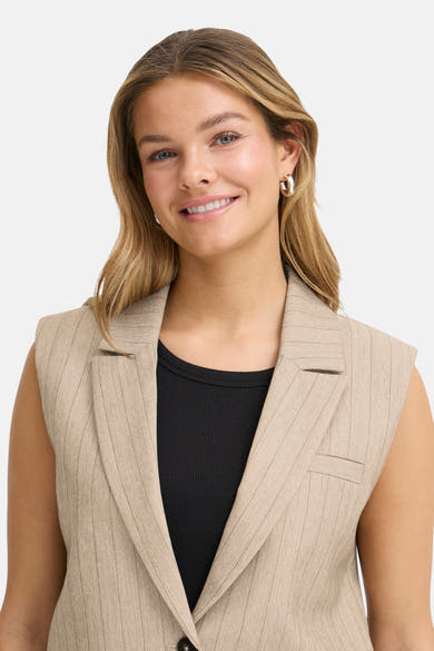 Beige mouwloos colbert van Fransa, met subtiel streepmotief, gedragen over een effen zwart T-shirt.