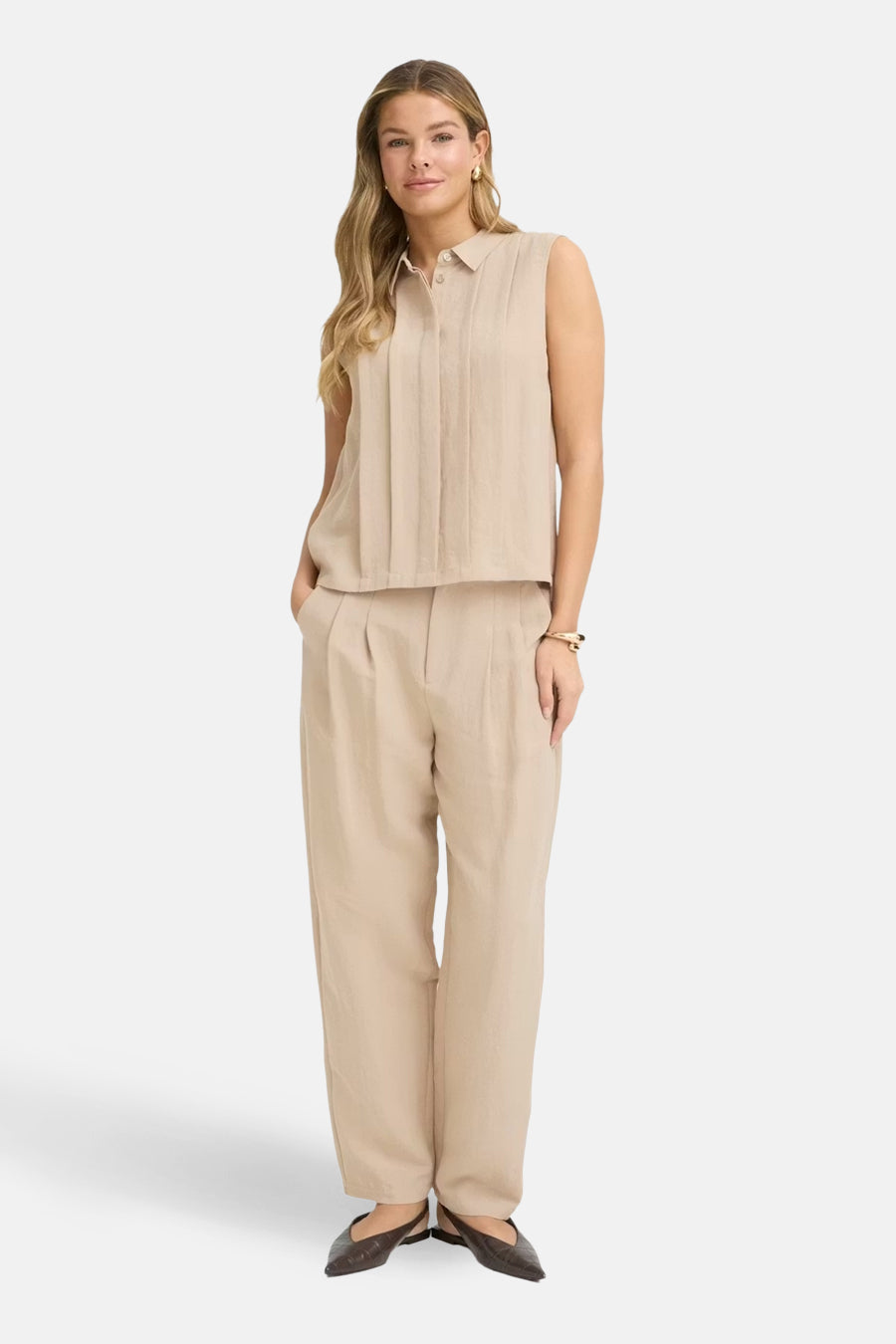 Chemisier beige sans manches de Fransa, avec un col, porté avec un pantalon beige et des chaussures marron.
