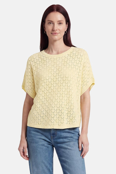 Pull col O jaune de Fransa en tricot ajouré à manches courtes, porté avec un jean et des boucles d'oreilles.
