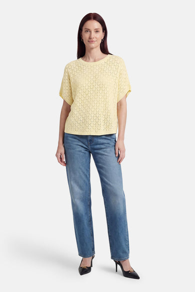 Pull jaune de Fransa en maille ajourée à losanges, col rond et manches courtes. Porté avec un jean bleu et des escarpins noirs.