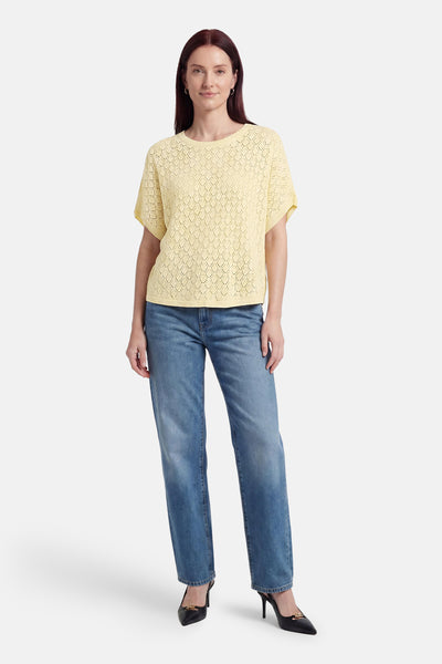 Pull jaune de Fransa en maille ajourée à losanges, col rond et manches courtes. Porté avec un jean bleu et des escarpins noirs.