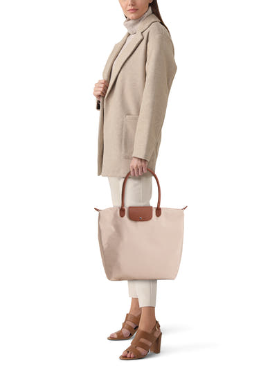 Sac à bandoulière beige de Fransa, avec poignées marron, porté avec un manteau beige et des chaussures à talons.
