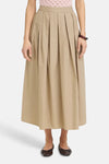 Lange beige rok van Fransa met elastische taille, van achteren gezien, gedragen met een roze top en bruine ballerina's.