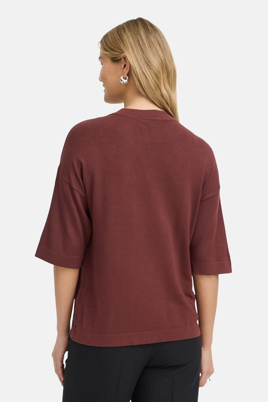 Burgundy ribbed knit round-neck sweater by Fransa, three-quarter sleeves, back view, model wearing black pants and silver hoop earrings