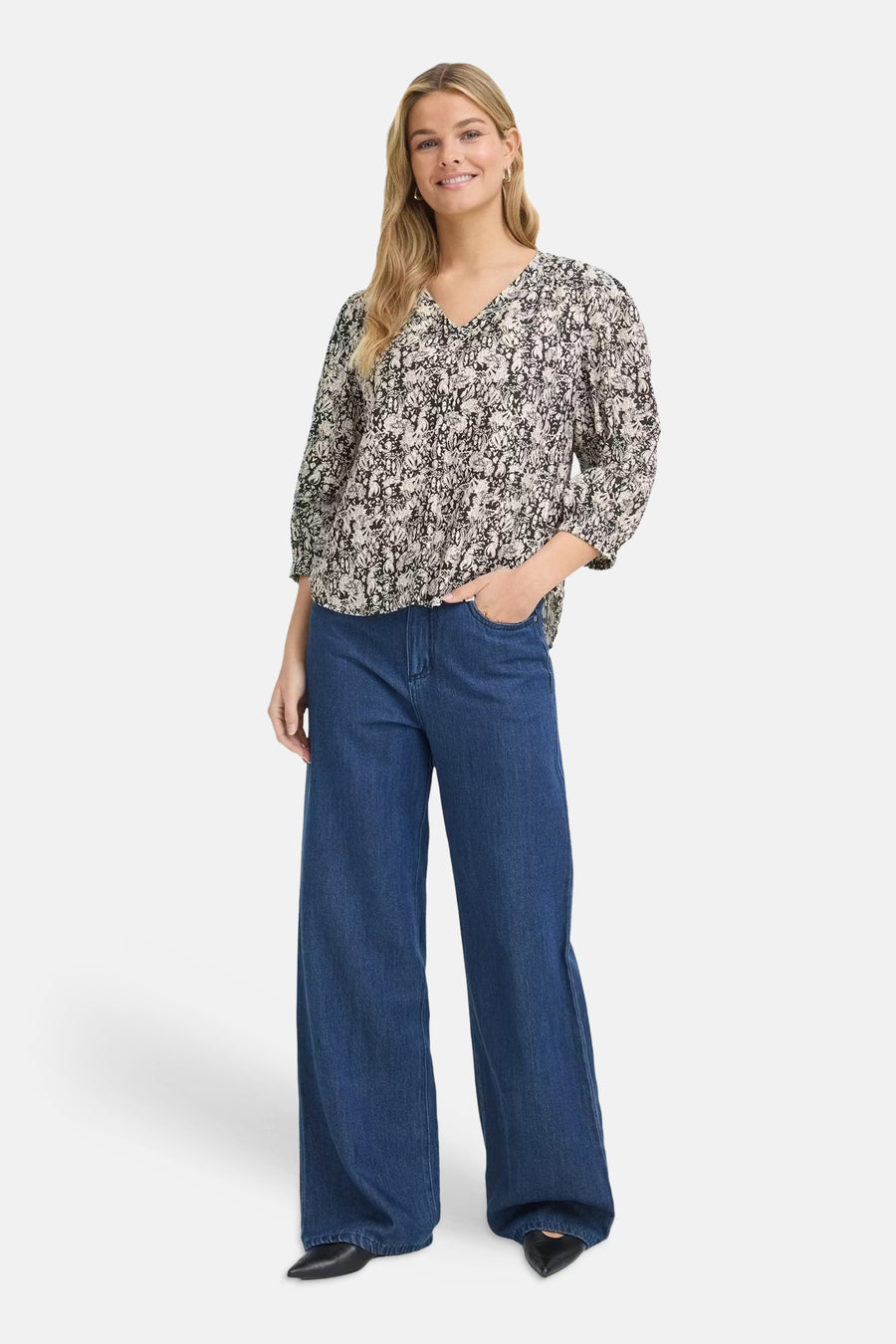 Multicolored short-sleeve blouse with floral print and V-neck, worn with blue wide-leg jeans and black pointed-toe shoes, front view.