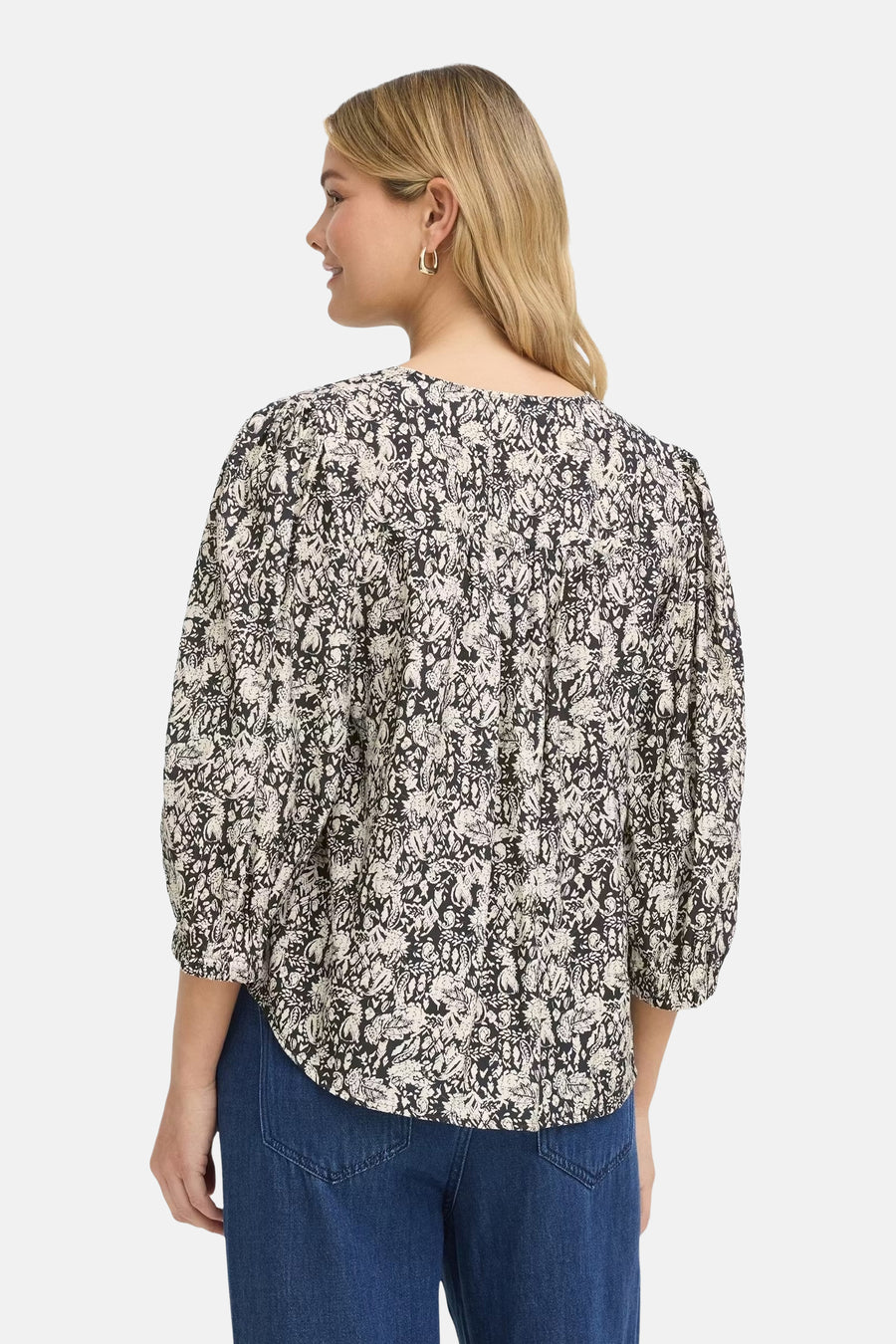 Multicolored short-sleeve blouse with black and white floral print, back view, featuring gathered shoulders and relaxed fit, worn with blue jeans.