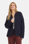 Gilet bleu marine en maille épaisse par Fransa®, boutonné avec poches et bordure contrastante, porté sur un haut blanc ajouré et pantalon bordeaux.