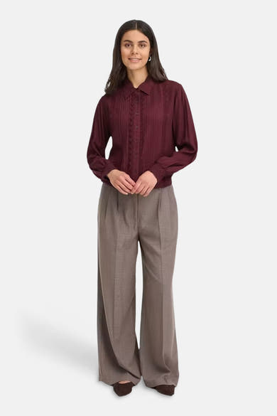 Bordeaux long-sleeve blouse with pleated front and lace detailing, worn with wide-leg trousers and brown heels, full-length front view
