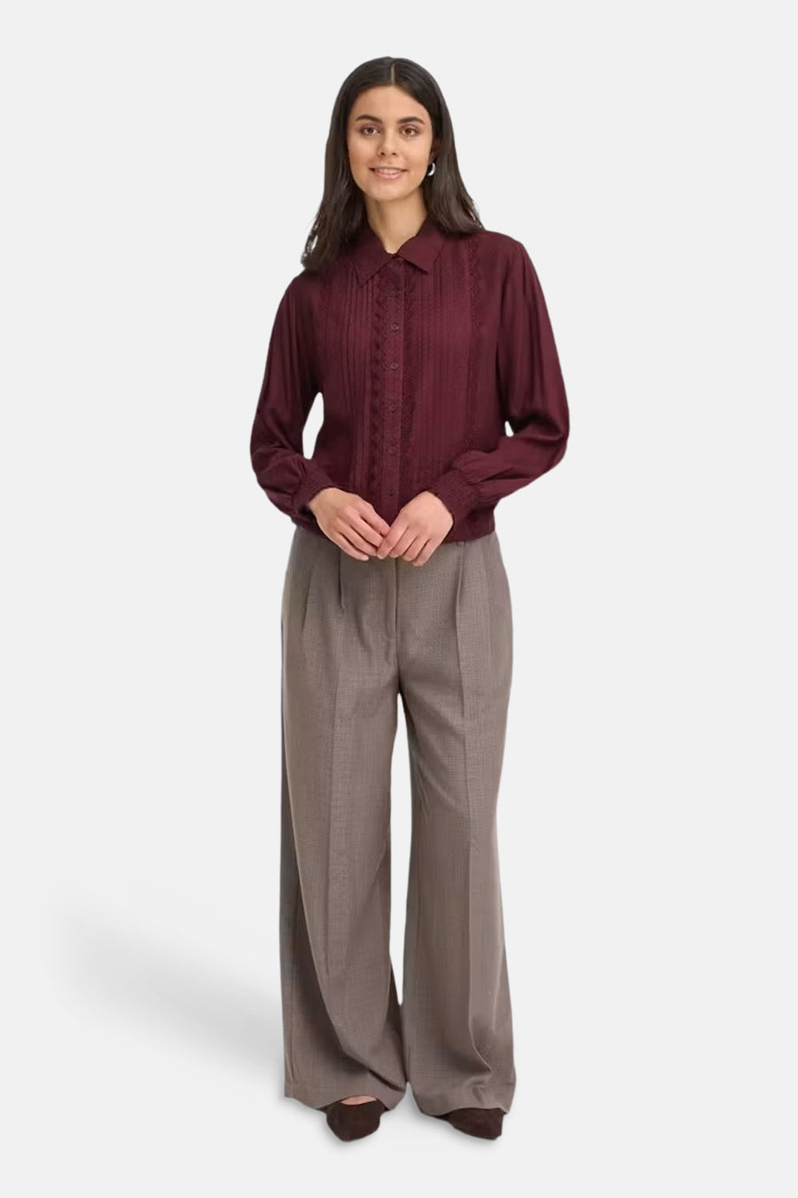 Bordeaux long-sleeve blouse with pleated front and lace detailing, worn with wide-leg trousers and brown heels, full-length front view