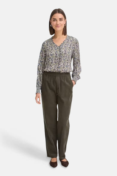 Multicolored long-sleeve blouse with floral pattern and ruffled V-neck, worn with olive green trousers and brown flats, front view