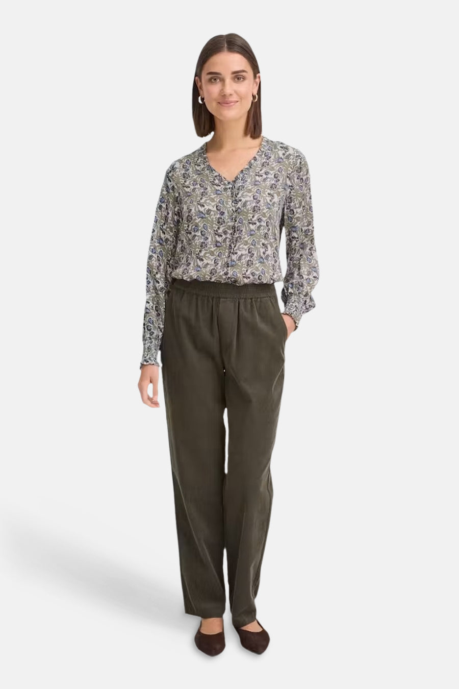 Multicolored long-sleeve blouse with floral pattern and ruffled V-neck, worn with olive green trousers and brown flats, front view