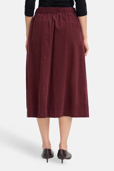 Burgundy corduroy midi skirt with elastic waistband, back view, worn with black top and heels
