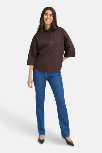 Brown long-sleeve blouse with button front and relaxed fit, worn with blue jeans and black heels, full-body front view
