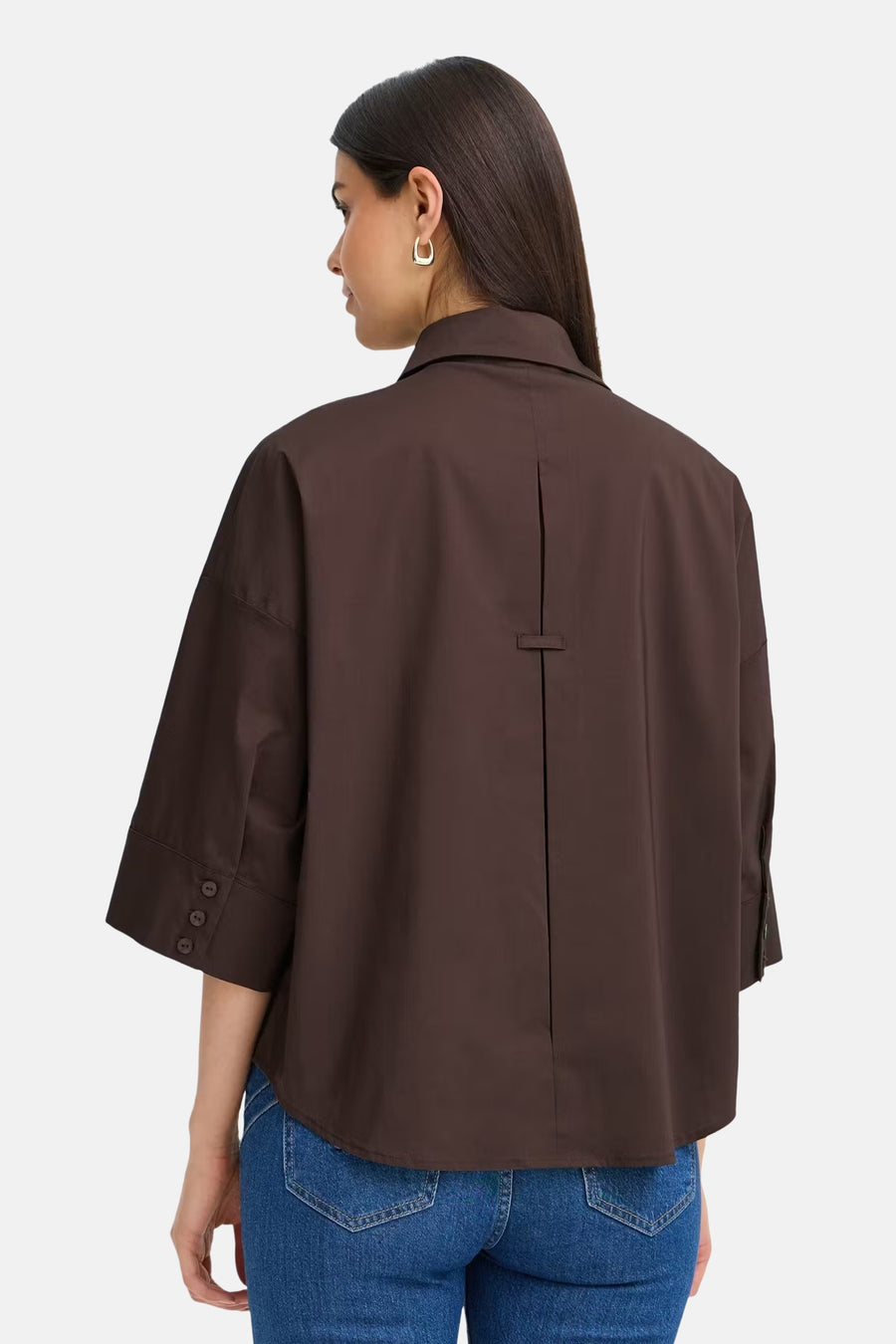 Brown long-sleeve shirt with back pleat and buttoned cuffs, worn with blue jeans, back view