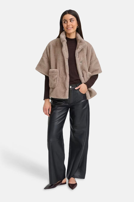 Beige fuzzy short coat with wide sleeves and front pockets, worn over dark brown top and black leather pants, full-length front view